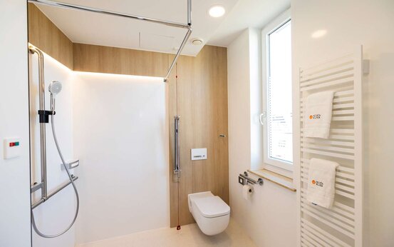 Modernes, barrierefreies Badezimmer mit ebenerdiger Dusche, Haltegriffen, wandhängender Toilette, Fenster und Handtuchheizkörper
