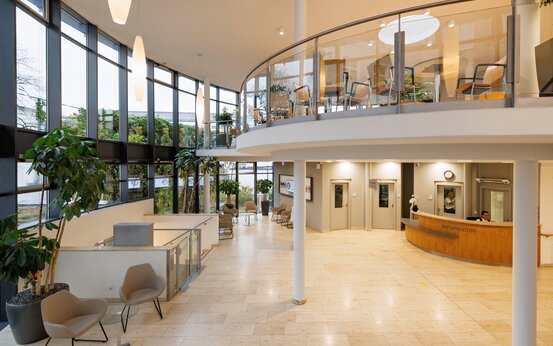 Heller, großzügiger Klinik-Eingangsbereich mit Informationstheke, Sitzgruppen und großen Fensterfronten.