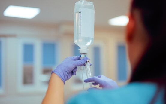 Medizinische Fachkraft mit blauen Handschuhen bereitet Infusion mit Spritze im Klinikraum vor