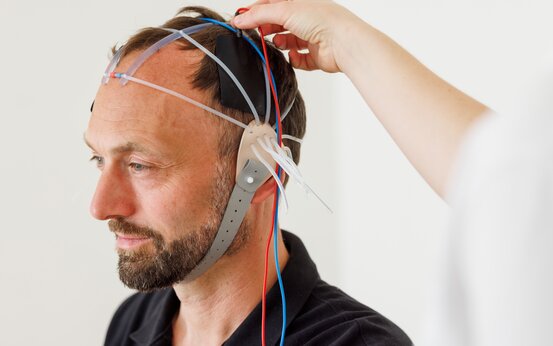 Medizinisches Personal bringt Patientin ein Gerät zur transkraniellen Gleichstromtherapie mit Kabeln am Kopf an