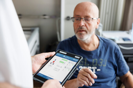 Arzt dokumentiert mit Tablet im Gespräch mit Parkinson-Patienten auf der neurologischen Station.