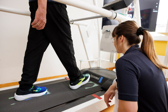 Physiotherapeutin begleitet Parkinson-Patient beim Gangtraining auf Laufband in moderner Klinik, Fokus Bewegungsförderung.