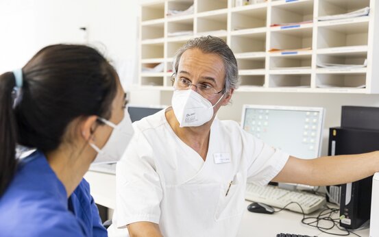 Arzt und medizinische Fachkraft gemeinsam im Gespräch an Schreibtisch