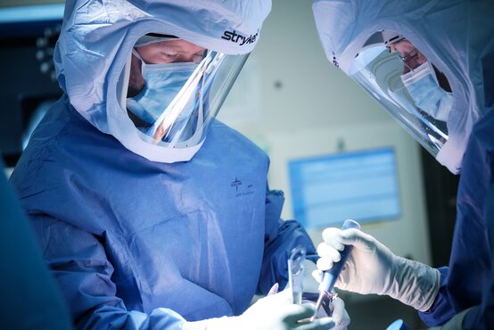 Zwei Mediziner in blauer OP-Kleidung und Gesichtsschutz operieren konzentriert im modernen Operationssaal