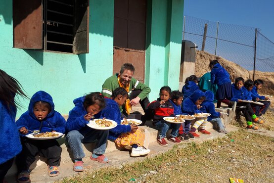 Kinder und ein Erwachsener essen gemeinsam auf einer Treppe vor einem Haus