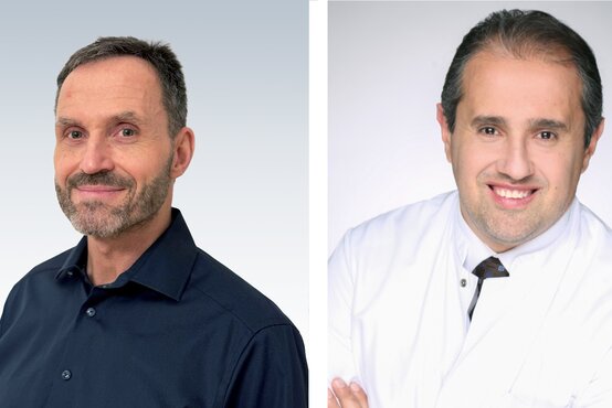 Zwei Männer nebeneinander, links im dunkelblauen Hemd mit Bart, rechts im weißen Arztkittel und Krawatte, beide vor hellem Hintergrund