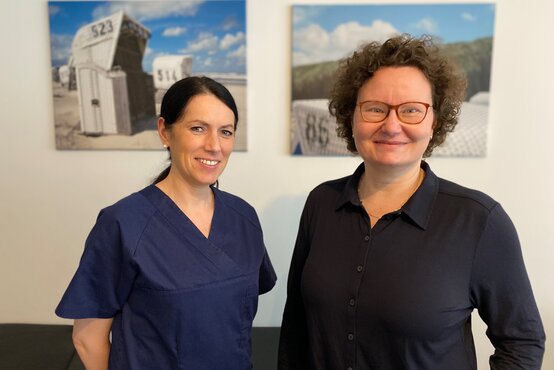 Zwei Frauen stehen nebeneinander vor weißer Wand mit Strandkorb-Bildern