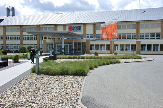Schön Klinik Neustadt mit großem Eingangsbereich, gepflegter Außenanlage und drei orangefarbenen Fahnen