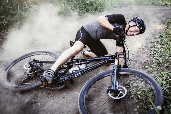 Radfahrer stürzt auf einem Waldweg und liegt mit dem Fahrrad auf dem Boden
