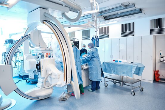 Mehrere Ärztinnen und Ärzte in steriler OP-Kleidung arbeiten im modernen Hybrid-Operationssaal