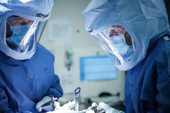 Zwei Personen in blauer OP-Kleidung und Gesichtsschutz führen Knieoperation im modernen Operationssaal durch