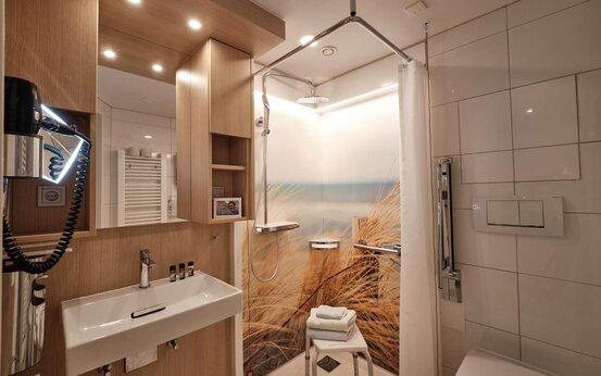 Barrierefreies Badezimmer mit Dusche, Duschhocker, Haltegriff, Waschbecken und Holzverkleidung