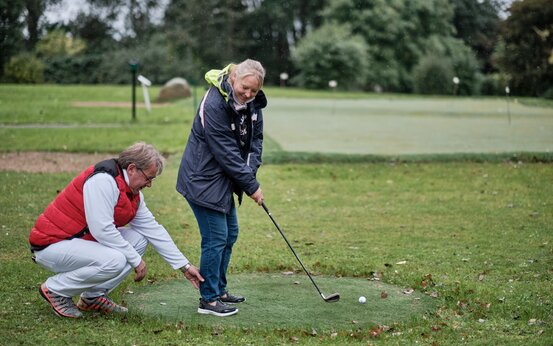 Therapeut hilft Patientin auf Golfplatz bei Golfübungen zur Therapie