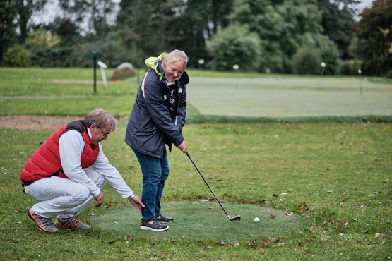 Therapeut hilft Patientin auf Golfplatz bei Golfübungen zur Therapie