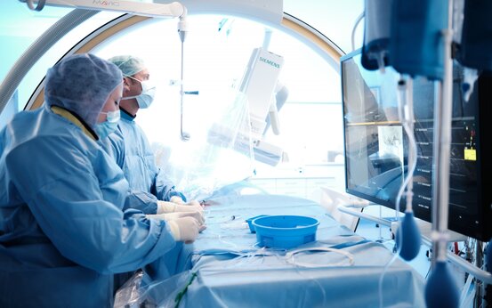 Zwei medizinische Fachkräfte in blauer OP-Kleidung bedienen medizinische Geräte im hellen Operationssaal