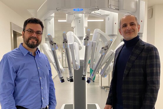 Zwei Männer vor medizinischem Roboter mit mehreren Armen im hellem Krankenhaus, Innovation in der Chirurgie