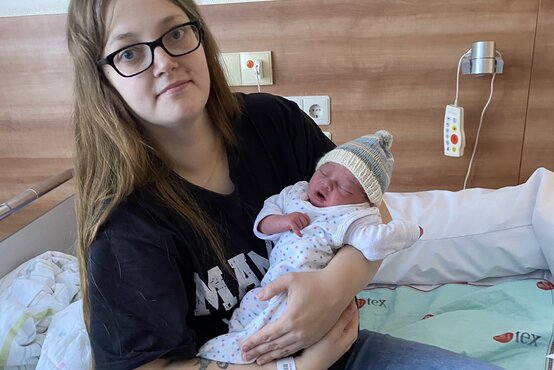 Junge Mutter mit Brille hält Neugeborenes im Krankenhausbett