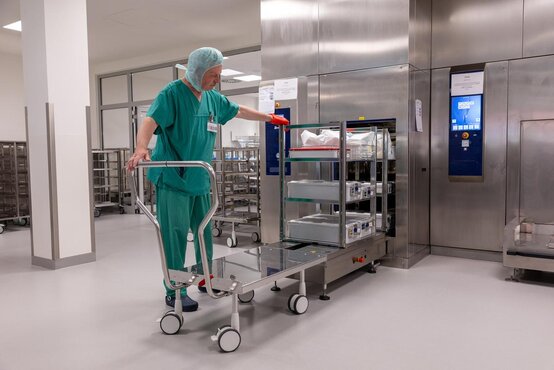 Mitarbeiterin der Zentralsterilisation schiebt Transportwagen mit Sterilgutcontainern zum Sterilisator