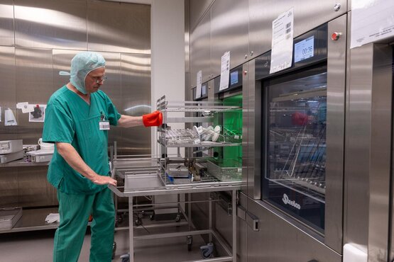 Mitarbeiter der Zentralsterilisation entnimmt gereinigte Instrumentensiebe aus Desinfektionsgerät