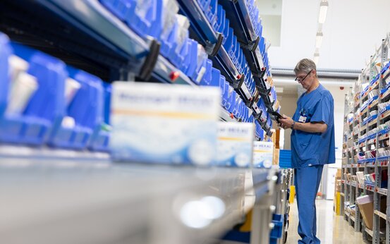 Mann in blauer Arbeitskleidung scannt Medikamente in Lagerregal mit vielen blauen Kisten
