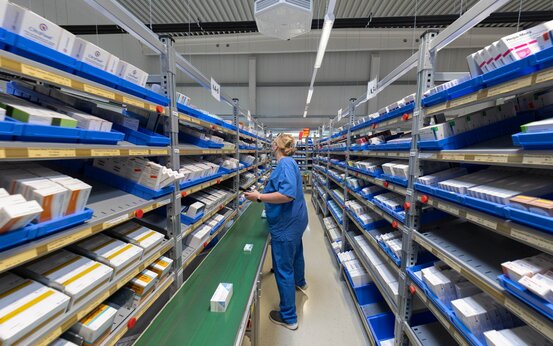 Mitarbeiterin sortiert Medikamente in moderner Apotheke, Arzneimittelregale im Hintergrund