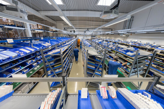 Zwei Mitarbeitende sortieren Medikamente in blauen Kisten im modernen Apothekenlager