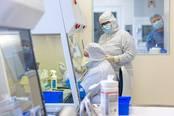 Zwei Personen in Schutzkleidung arbeiten an Werkbank im Reinraumlabor für Zytostatika-Herstellung