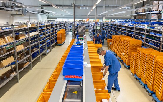 Mitarbeiter kommissioniert Medikamente in moderner Apotheke, Transportboxen und Regale in der Klinikapotheke