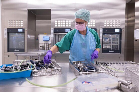 Mitarbeiterin in Schutzkleidung sortiert in der AEMP chirurgische Instrumente in Edelstahlkörben zur Reinigung und Desinfektion
