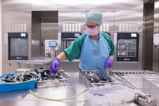 Mitarbeiterin in Schutzkleidung sortiert in der AEMP chirurgische Instrumente in Edelstahlkörben zur Reinigung und Desinfektion