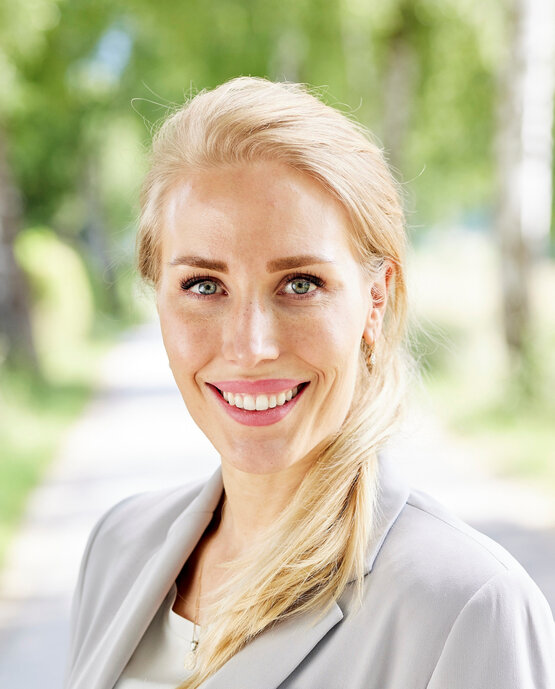 Porträt von Dr. Sophie Giessner, junge Frau mit blondem Haar im hellen Blazer, draußen vor grünem Hintergrund