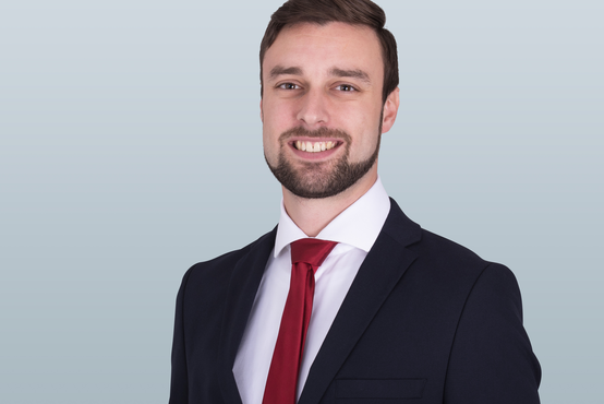 Porträt von Florian Breitenstein, lächelnd im weißen Hemd vor neutralem Hintergrund