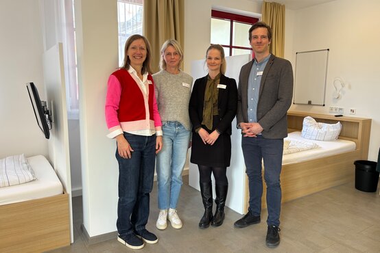 Vier Personen mit Namensschildern stehen lächelnd im hellen Patientenzimmer des Jugendhauses der Schön Klinik Roseneck