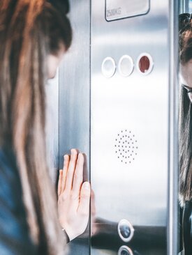 Frau lehnt mit der Hand an die Wand eines Fahrstuhls und zeigt Anzeichen von Angst oder Panik