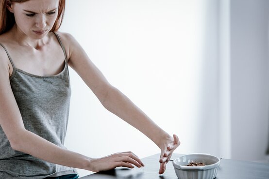 Junge Frau mit langen roten Haaren schiebt kleine weiße Schüssel mit Essen von sich weg, angespanntes Gesicht