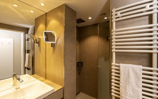 Modernes Komfortzimmer-Bad der Schön Klinik Roseneck mit ebenerdiger Dusche, Waschbecken und beleuchtetem Spiegel