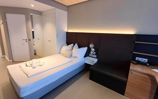 Modernes Einzelzimmer der Schön Klinik Roseneck mit Einzelbett, Sitzbank, Schreibtisch, weißen Schränken und Holzdecke