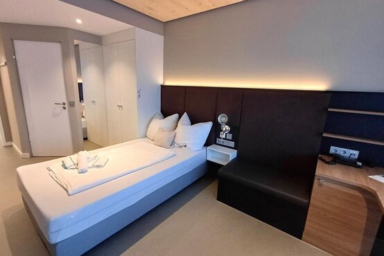 Modernes Einzelzimmer der Schön Klinik Roseneck mit Einzelbett, Sitzbank, Schreibtisch, weißen Schränken und Holzdecke