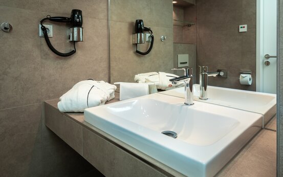 Modernes Bad der Schön Klinik Roseneck mit großem Spiegel, Waschbecken, Bademantel und Wandfön