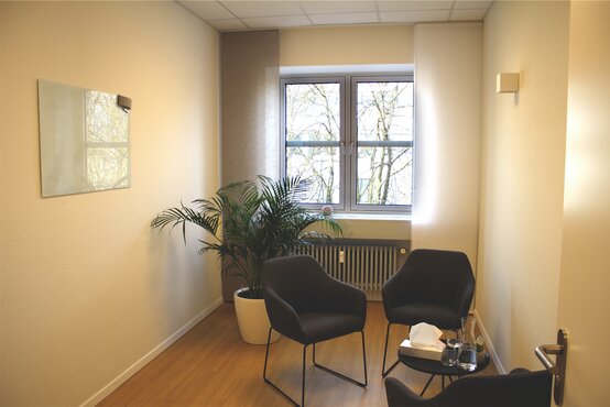 Modernes Zimmer in der Schön Klinik Roseneck, drei Stühlen an Tisch und großem Fenster, helle und freundliche Atmosphäre