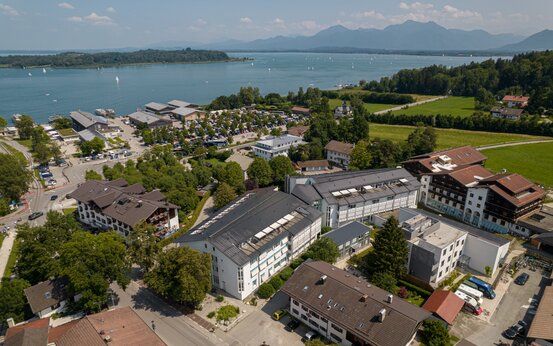 Luftaufnahme der Schön Klinik Roseneck vor dem Chiemsee mit Segelbooten, Alpenpanorama, Parkplatz und grüner Umgebung