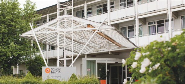 Eingangsbereich der Schön Klinik Roseneck mit weißer Fassade, Glasüberdachung und Schild „Haupteingang“