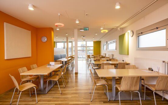 Heller Speisesaal der Schön Klinik Roseneck mit Holzboden, Holztischen, großen Fenstern und orangefarbener Wand