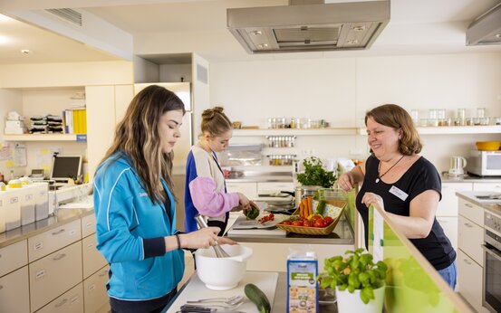 Drei Frauen schneiden gemeinsam Gemüse in moderner Küche der Schön Klinik Roseneck