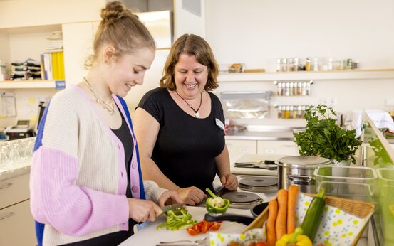 Zwei Frauen schneiden gemeinsam frisches Gemüse in moderner Küche der Schön Klinik Roseneck