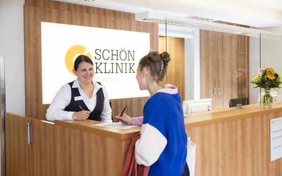 Mitarbeiterin der Schön Klinik Roseneck spricht am Empfangstresen mit Besucherin