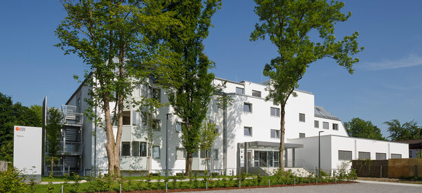 Modernes Klinikgebäude Haus Rosenheim mit weißer Fassade, Zugang, Grünflächen und Bäumen