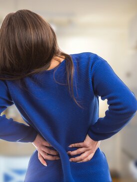 Frau in blauem Pullover hält sich den schmerzenden Rücken