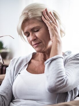 Frau mit blonden Haaren und Brille in der Hand hält sich die Hand ans Ohr