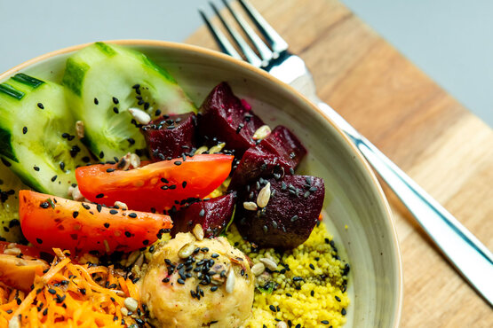 Bunte Bowl mit Tomaten, Gurken, Roter Bete, Hummus, Couscous, Karotten und Saaten auf Holztisch